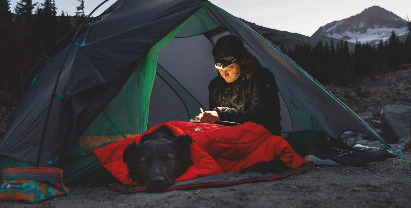 Alex writes in his trail diary with Raya by their tent.