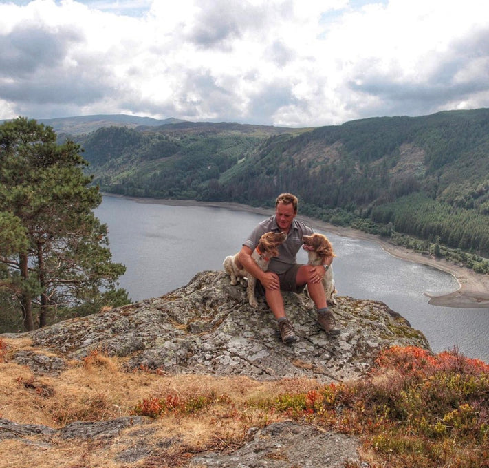A man and his two Springer Spaniel dogs sit on a cliff at the Lake District in England. 