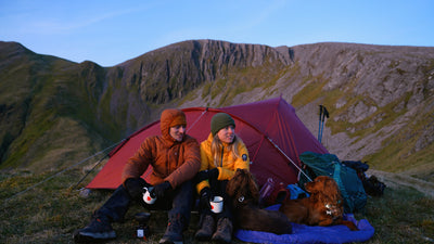 Man and woman sitting in front of tent next to two dogs