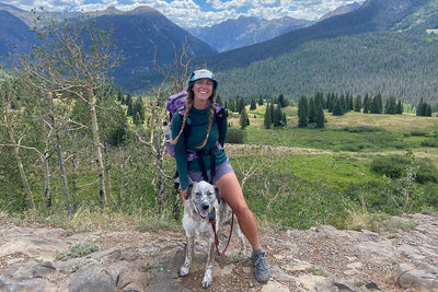 A woman stands with her dog in the mountains of Colorado.