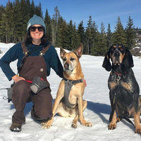 Laura with her two dogs sit on the snow together.