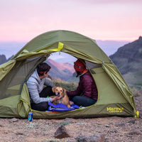 Two women sit in tent with dog at sunset on rocky hill in Steens Mountains.